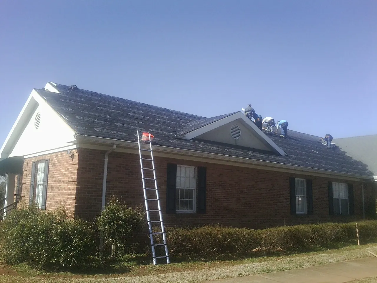 Crew tearing shingles off a brick ranch roof with a ladder set — Emergency Roof Repair work by our crew in Mount Pulaski