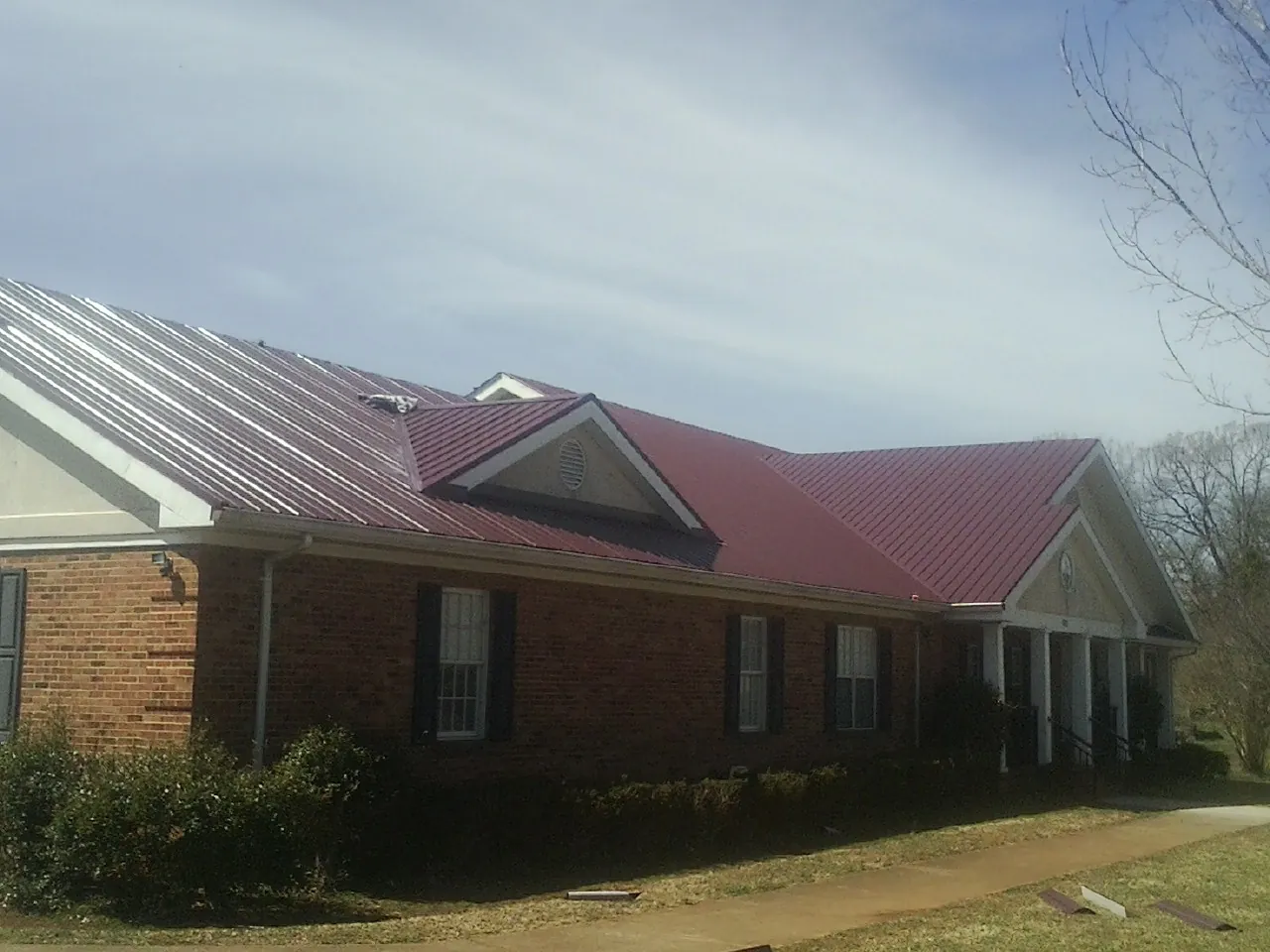 Red metal roof with gabled entries on a long brick building, from a Hail Damage Roof Repair job in Mount Pulaski