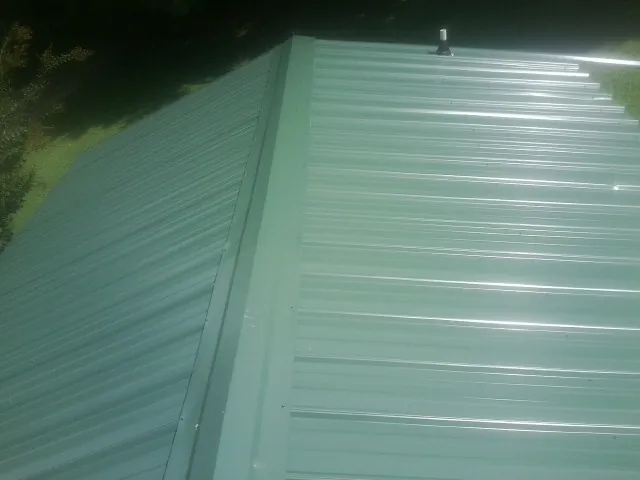New green metal panels meeting at the ridge of a roof — Flat Roof Repair work by our crew in Mount Pulaski