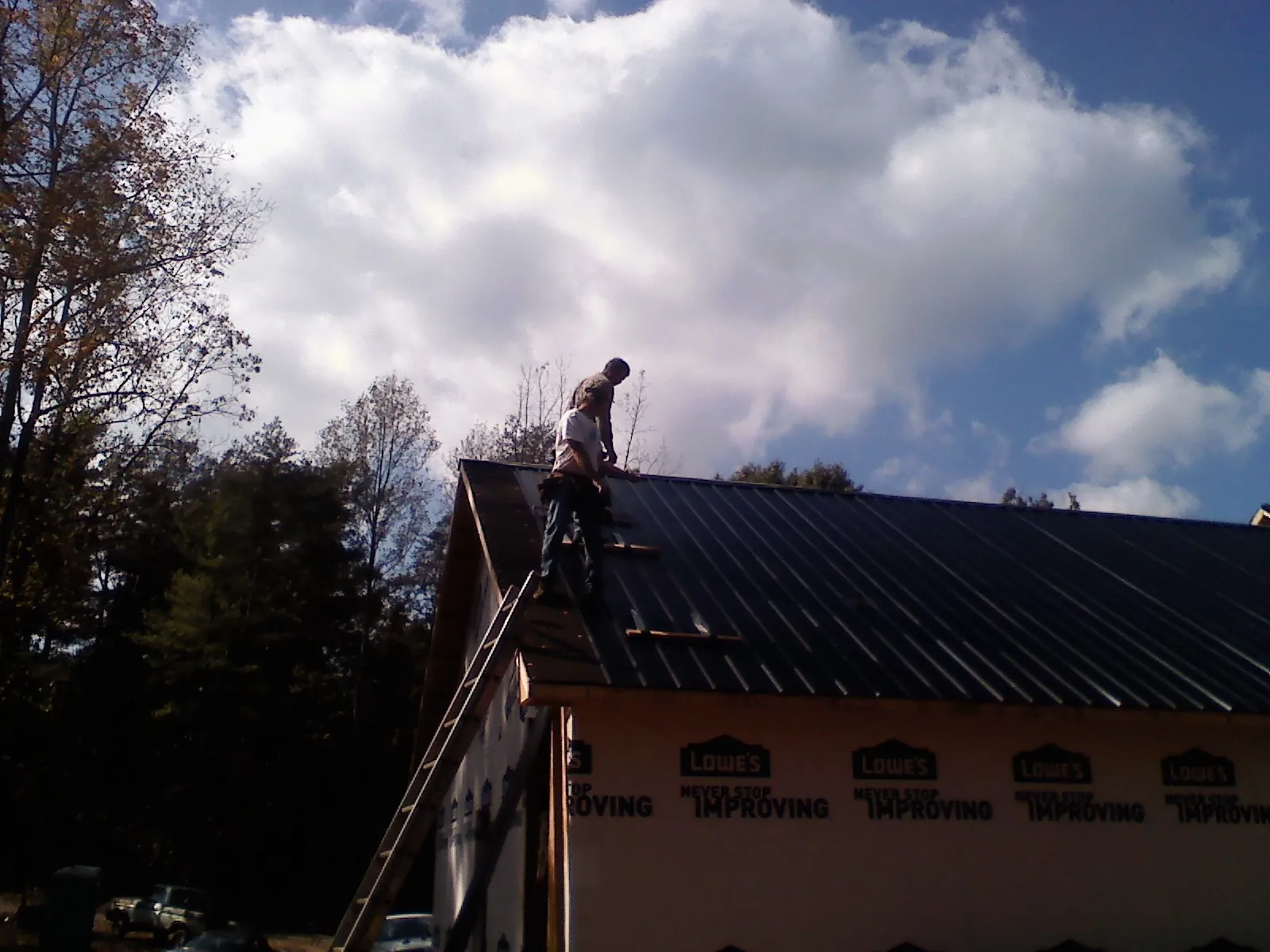 Roofer fastening dark metal panels high against a cloudy sky, from a Roof Inspection job in Mount Pulaski