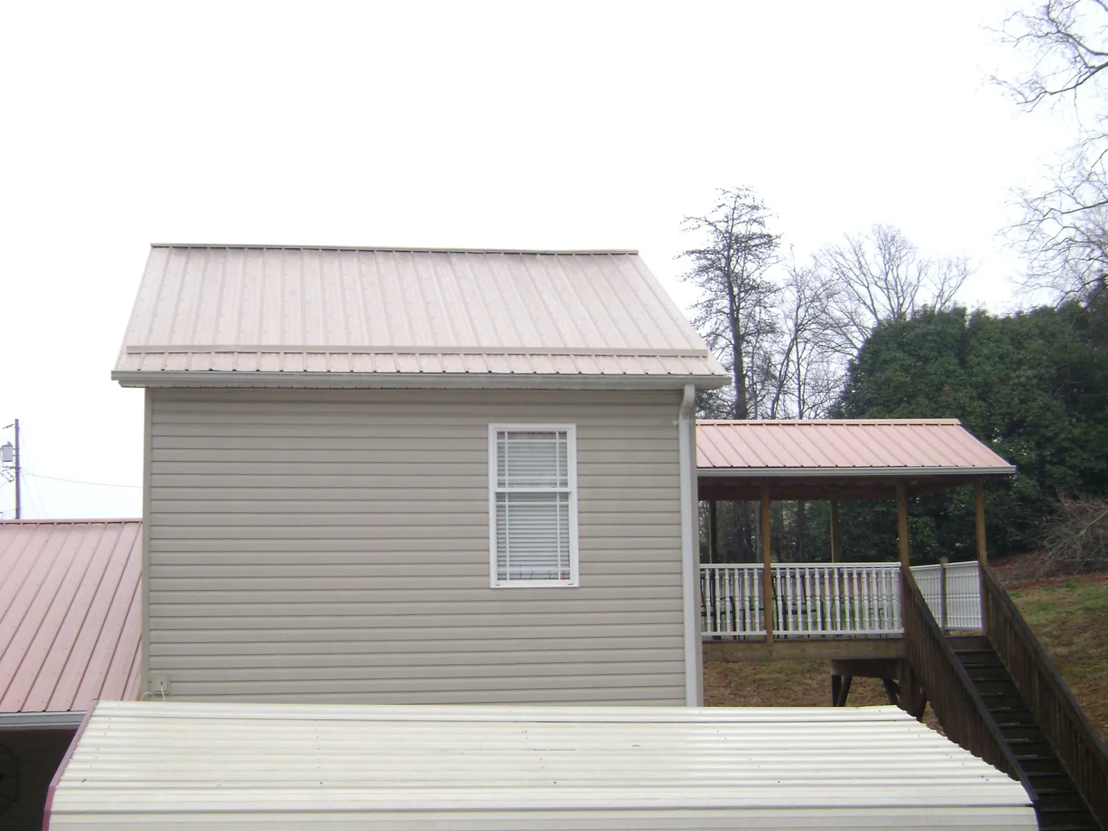 Tan metal roofs on a two story addition and attached porch, from a Roof Replacement job in Mount Pulaski